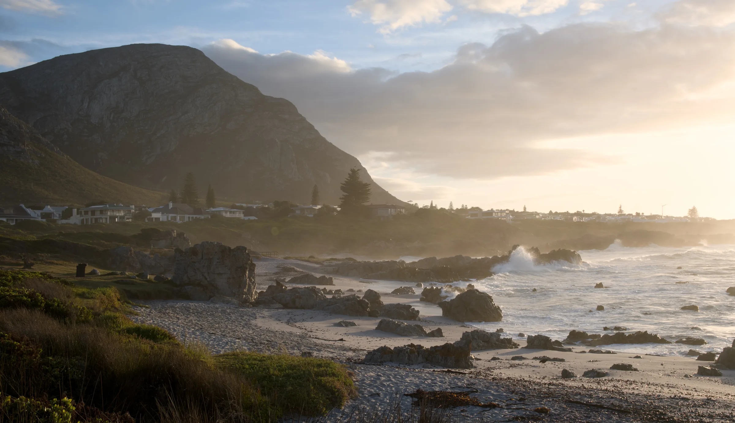 Rocky coastline at golden hour with waves crashing and mountains rising behind Hermanus